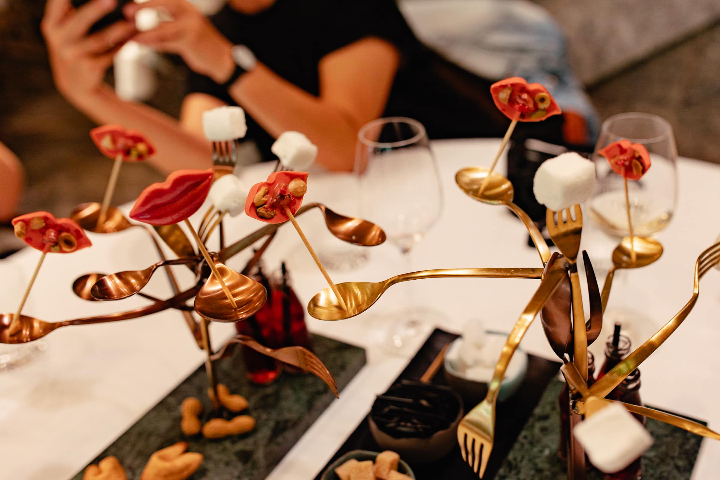 Auf goldenen Gabeln und Löffeln gesteckte Marshmallows und rote Schokolade in Lippenform als Dessert