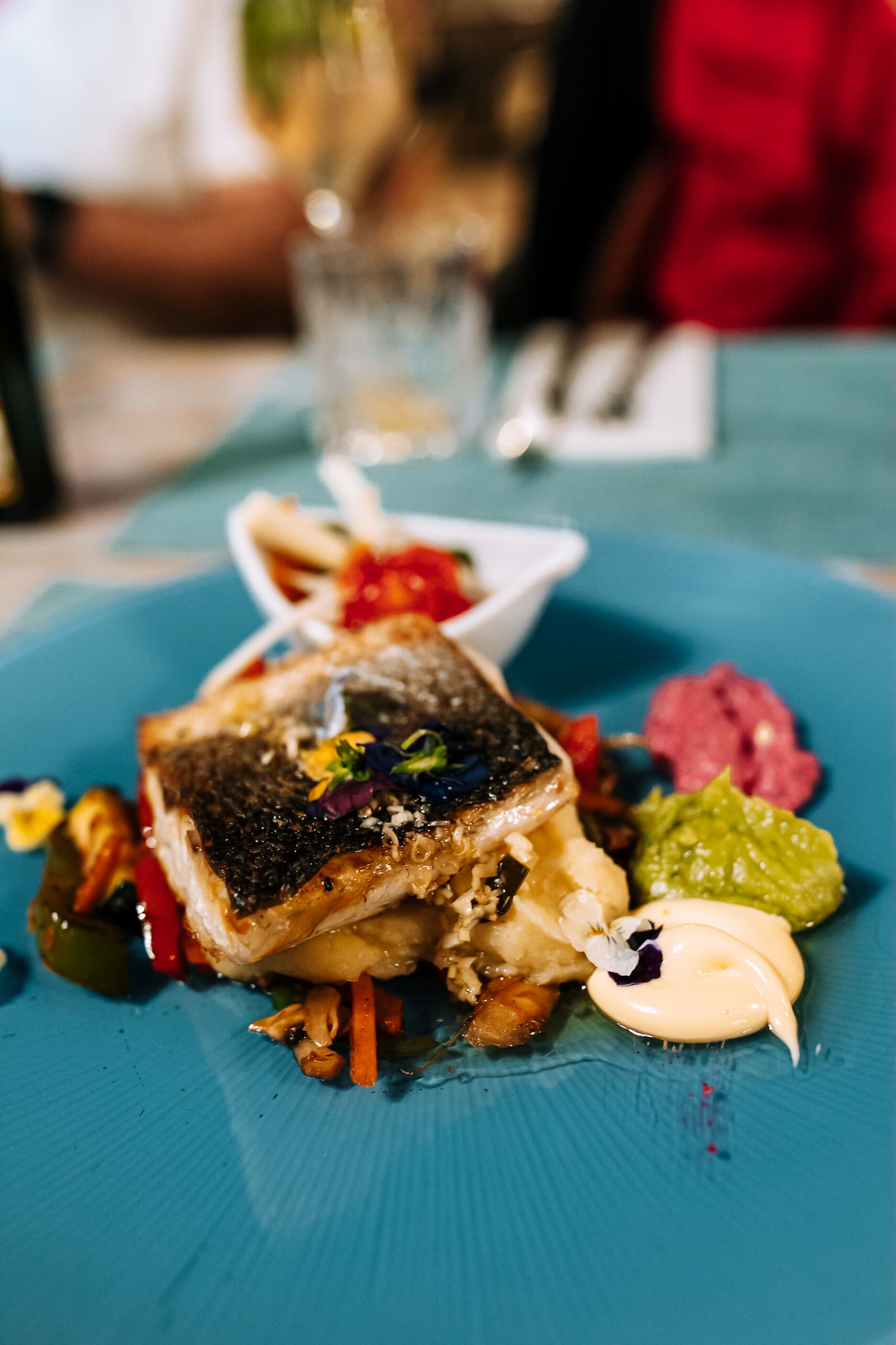 Fisch mit verschiedenen Dips und Blütendekoration auf blauem Teller im Siso Beach Mallorca