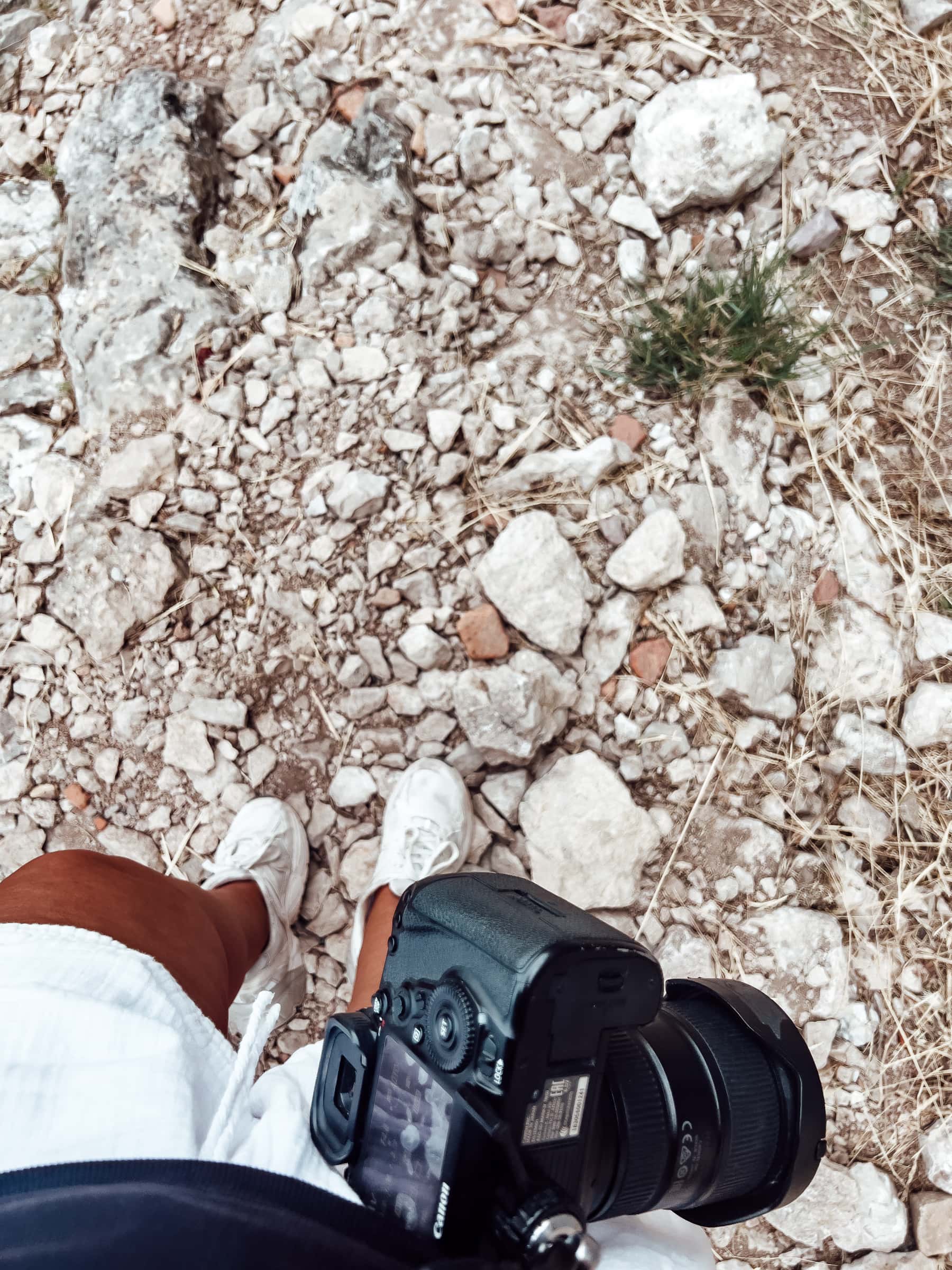 Person hält Kamera auf steinigem Boden.