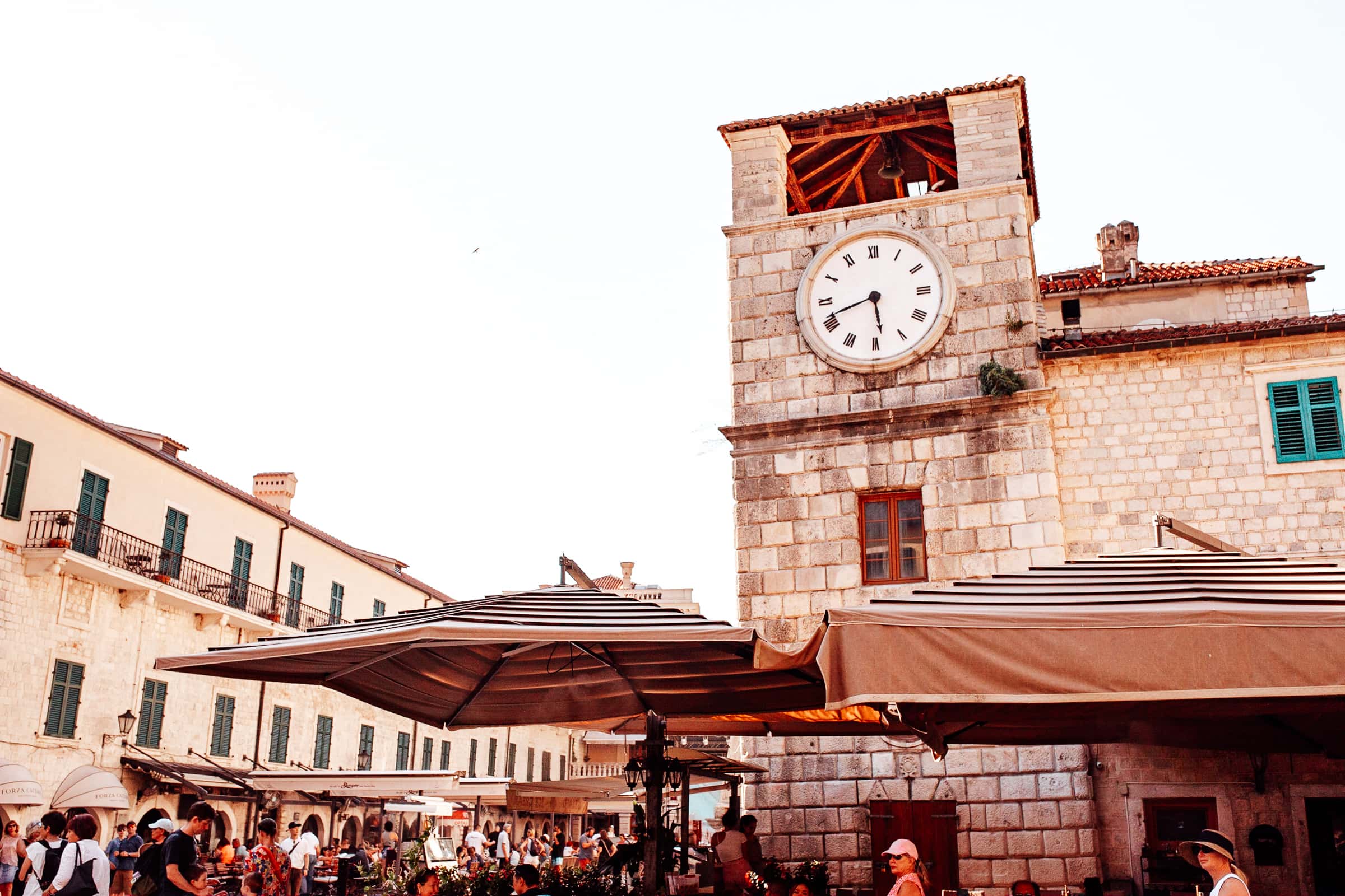 Marktplatz in Kotor mit Uhrturm, Menschen, Cafés.