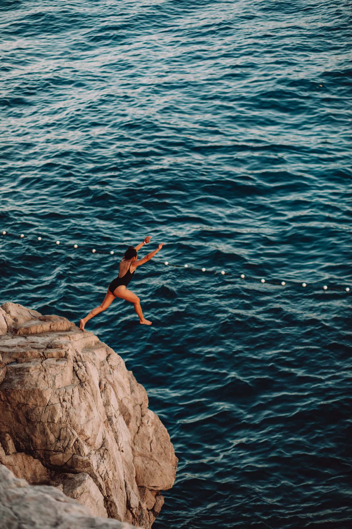 Person springt von Klippe ins Meer.