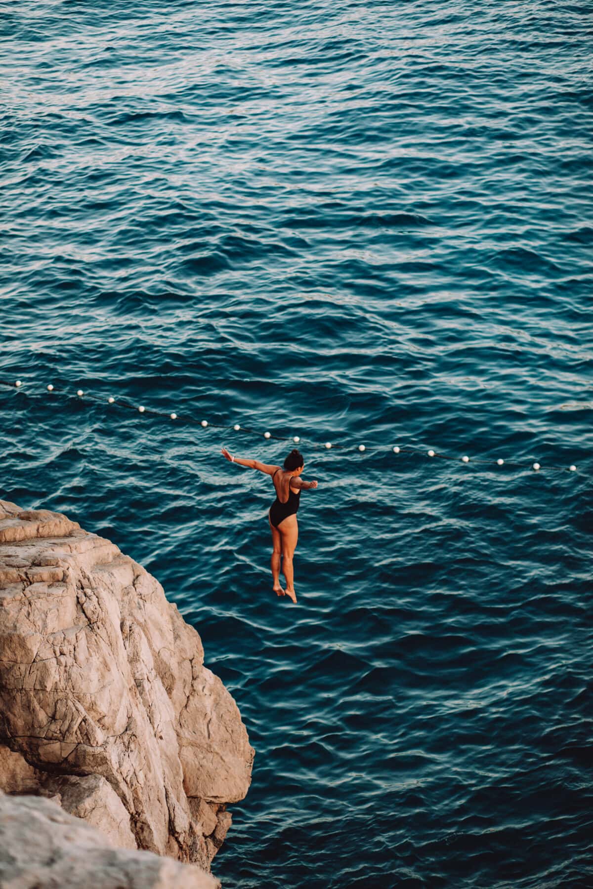Person springt von Klippe ins Meer.