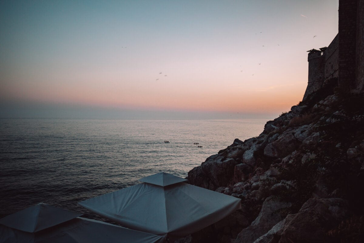 Sonnenuntergang am Meer mit Felsen und Sonnenschirmen.