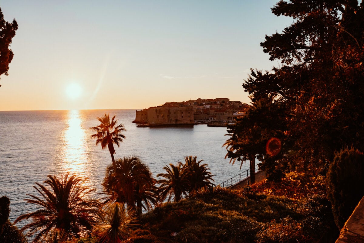 Sonnenuntergang über historischer Küstenstadt mit Palmen.