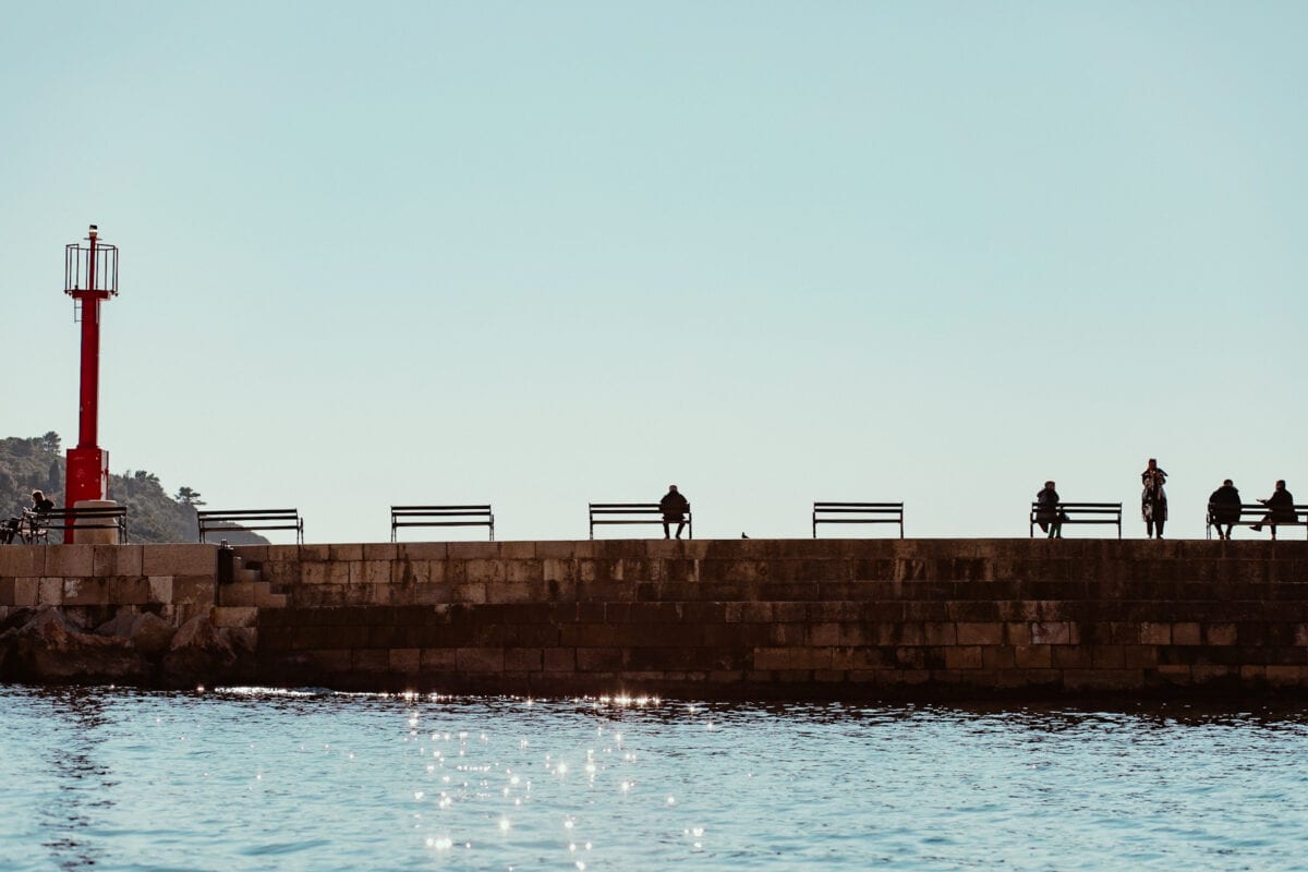 Menschen auf Hafenmole bei Sonnenuntergang