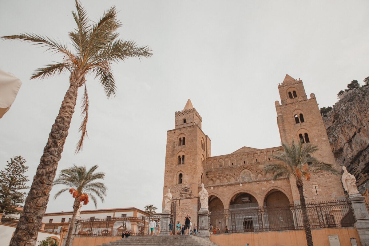 Normannische Kathedrale von Cefalu in Sizilien mit Palmen bei Tageslicht.