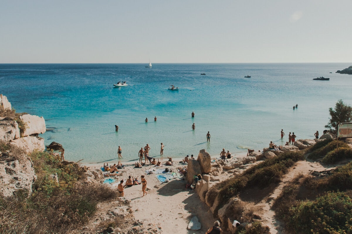 Belebter Strand mit kristallklarem Wasser und Booten.