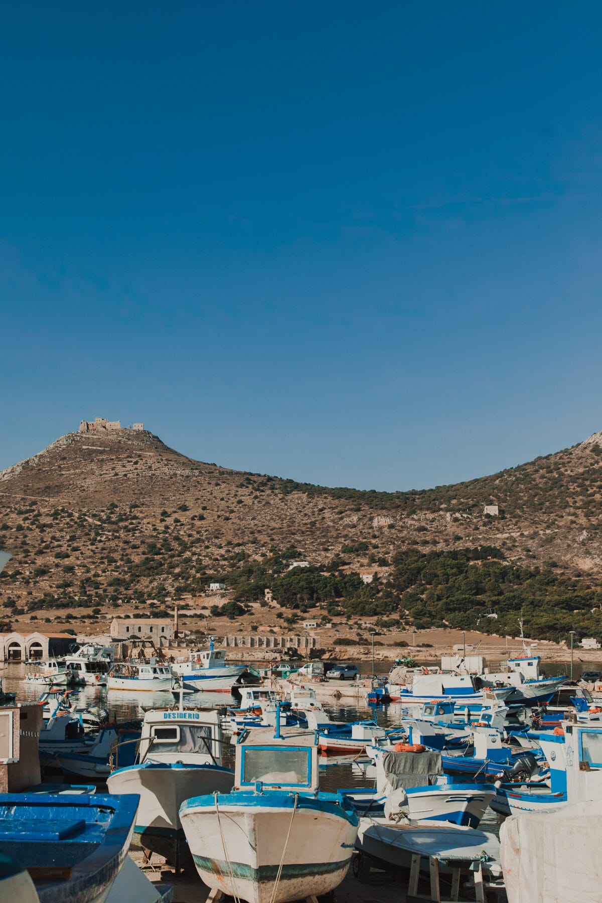 Hafen mit Booten und Burg auf Hügel.