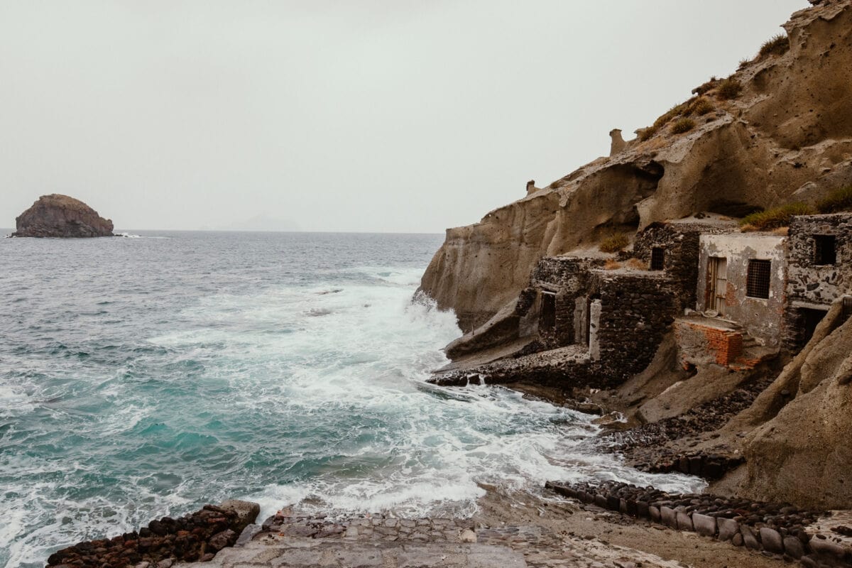 Felsige Küste mit alten Ruinen und Wellen.