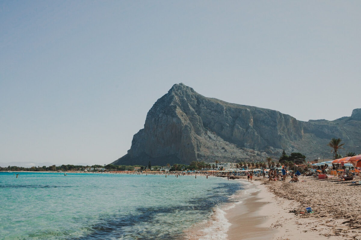 Belebter Strand mit Bergpanorama und klarem Wasser