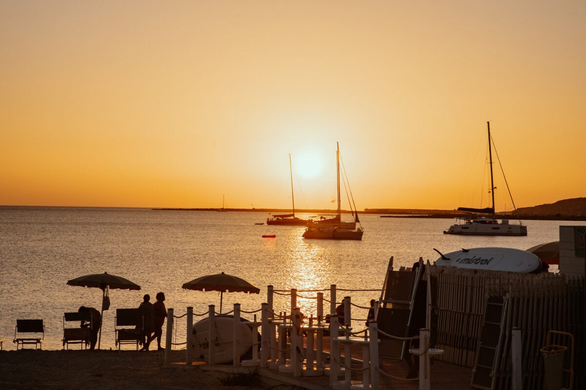 Sonnenuntergang am Meer mit Segelbooten und Strandbesuchern.