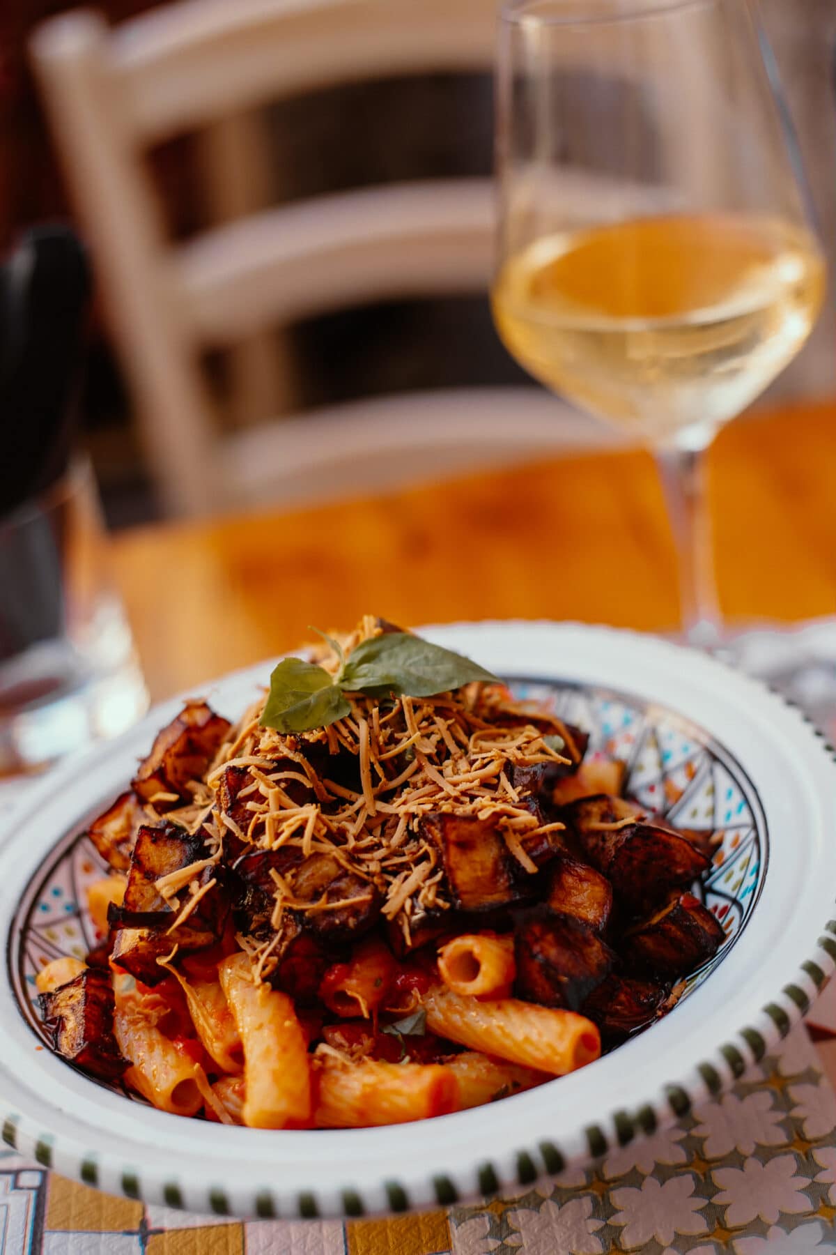 Teller Pasta mit Auberginen und Weinglas.