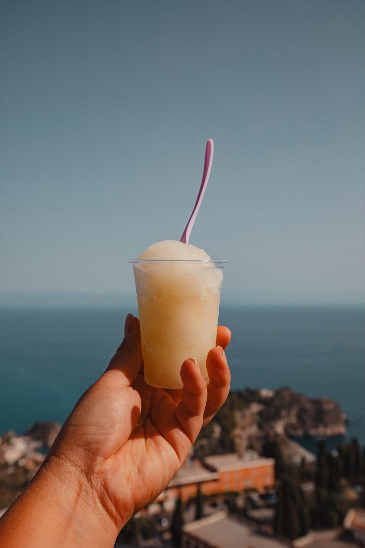 Hand hält Granita mit Meerblick.