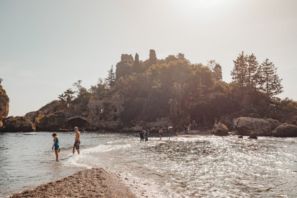 Menschen am sonnigen Strand mit historischen Ruinen.