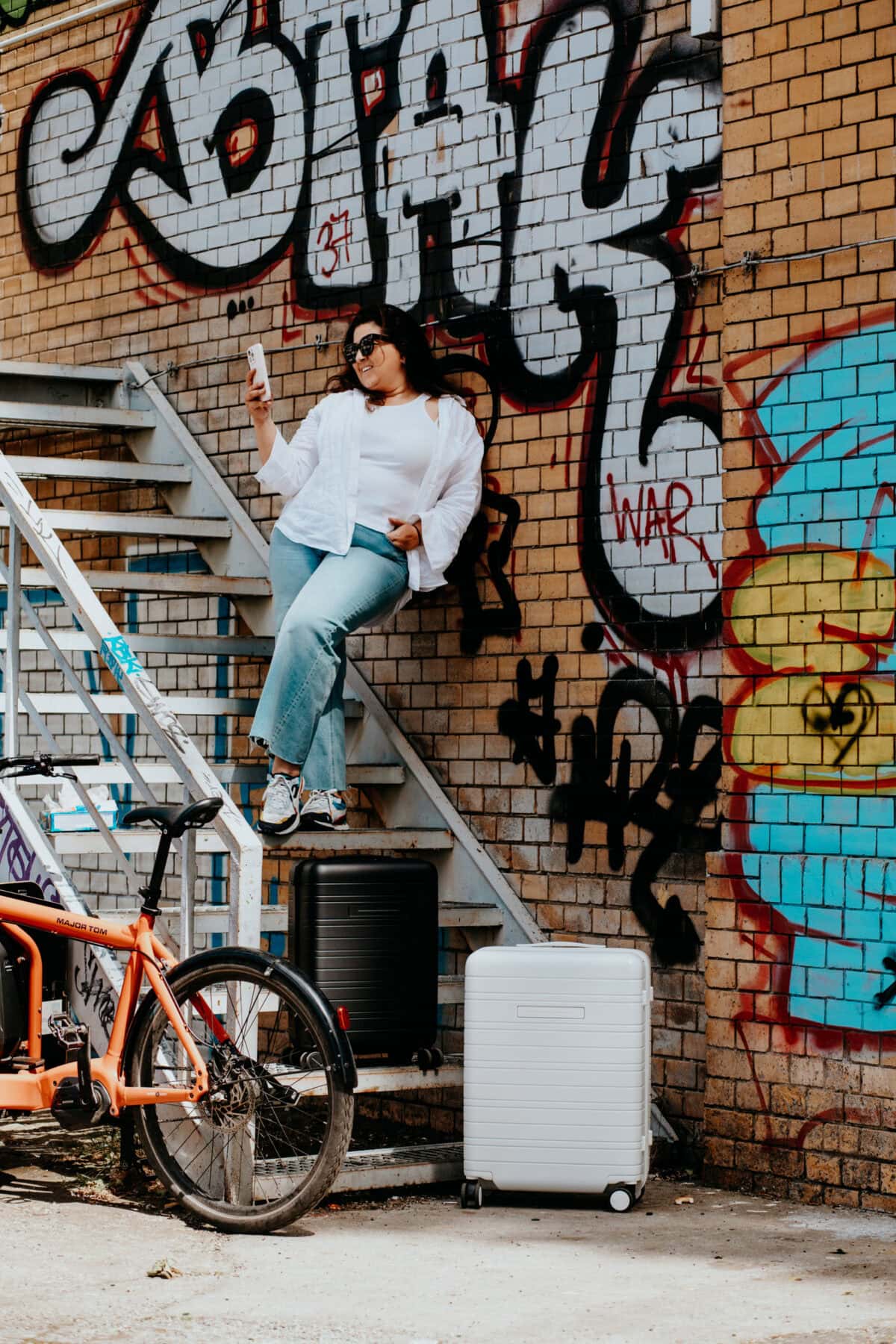 Frau macht Selfie vor Graffiti-Wand und zwei Koffer im Vordergrund.