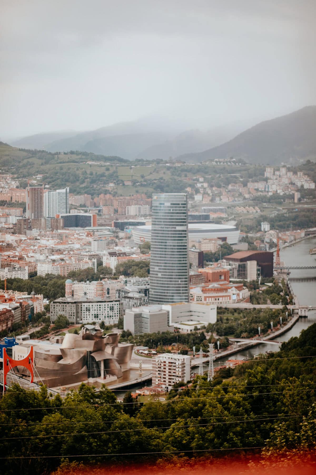 Stadtbild mit moderner Architektur und grünen Hügeln.