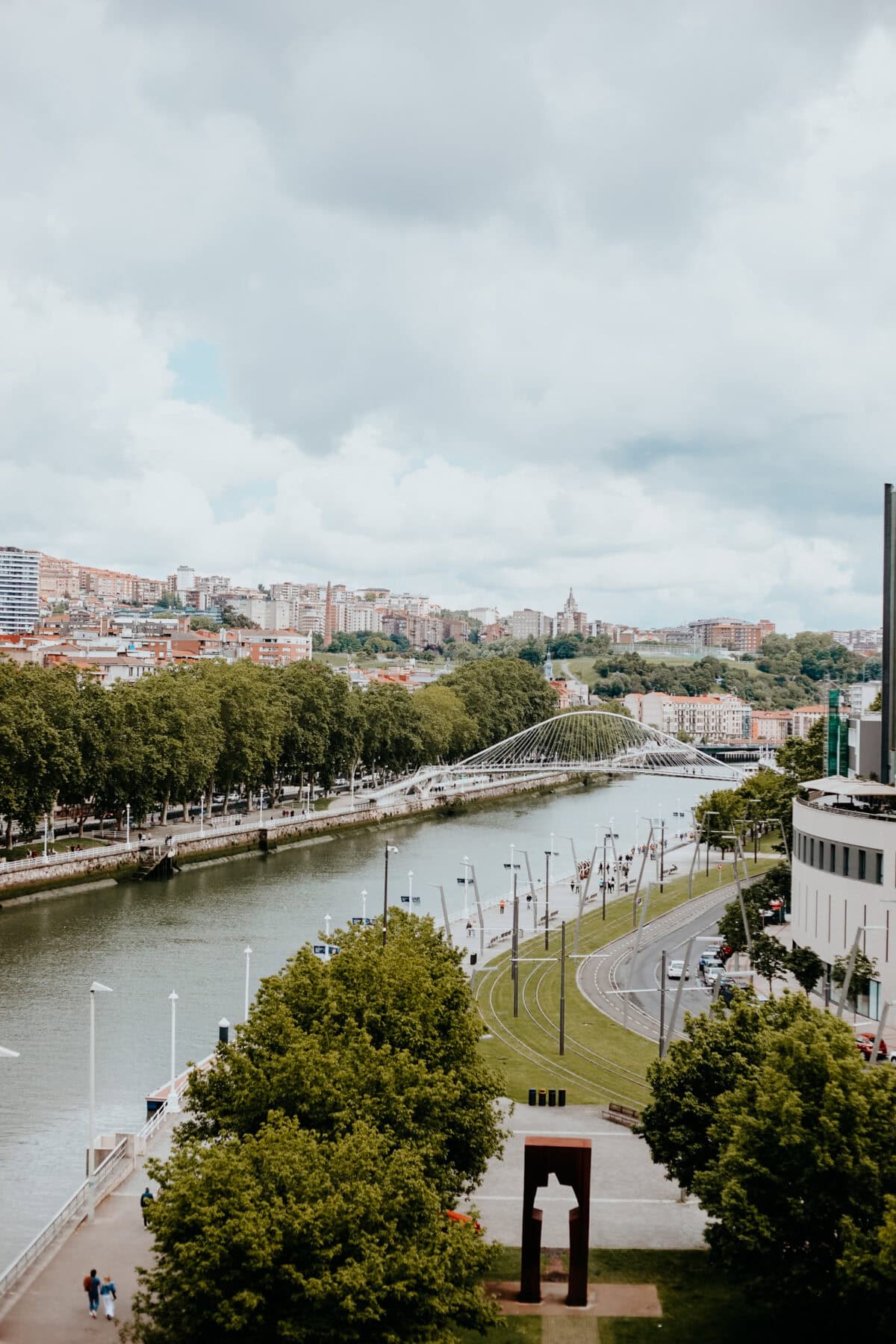Blick auf Flussufer und moderne Brücke in Stadtlandschaft.