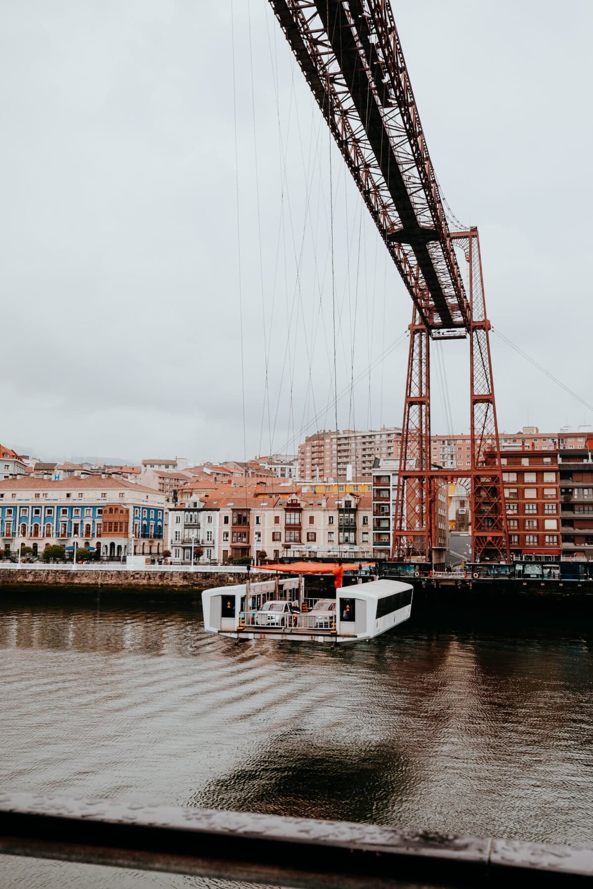 Brücke über Fluss mit Fähre und bunten Häusern.