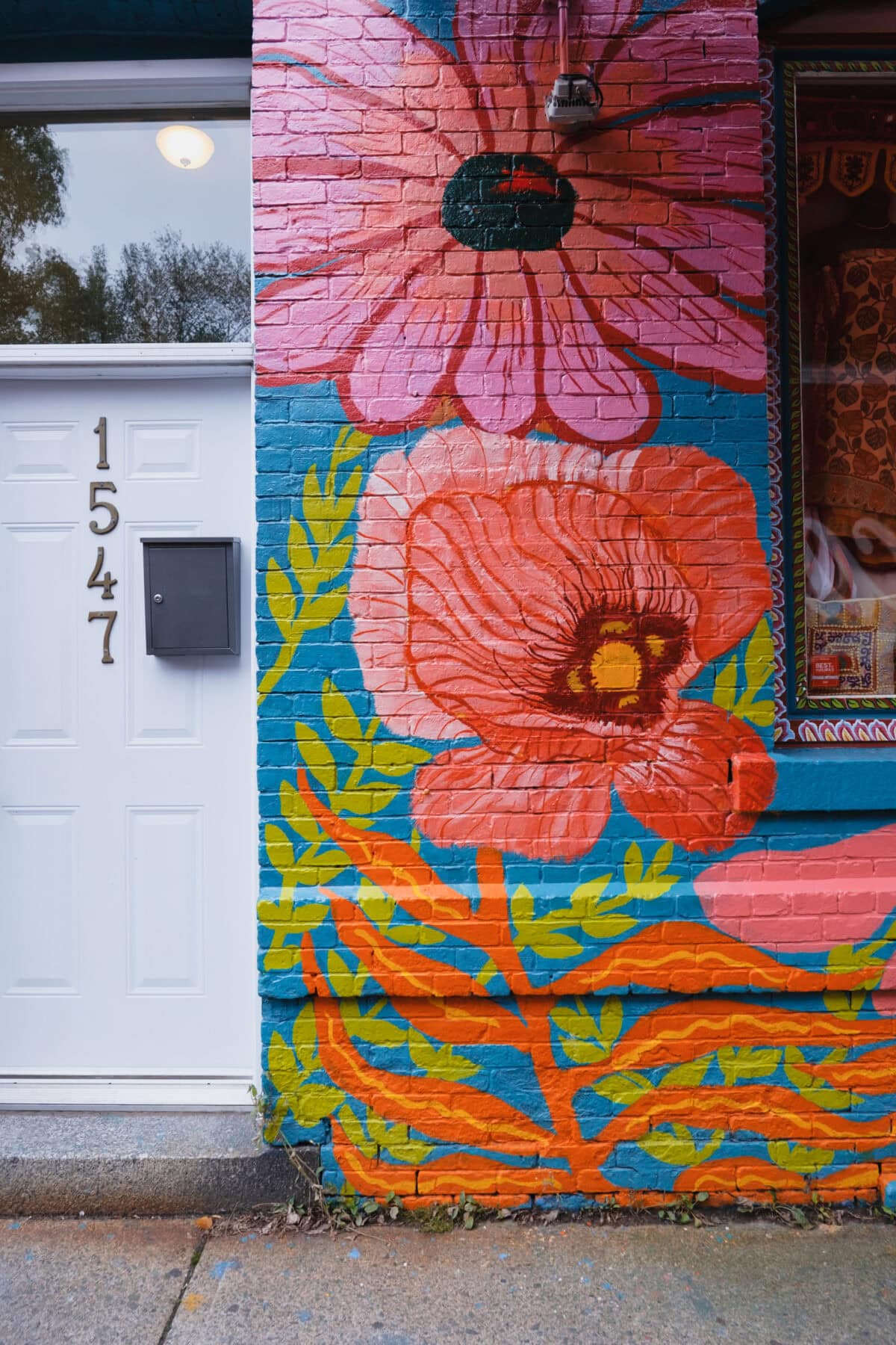 Buntes Blumenwandgemälde neben weißer Haustür, Hausnummer 1547.