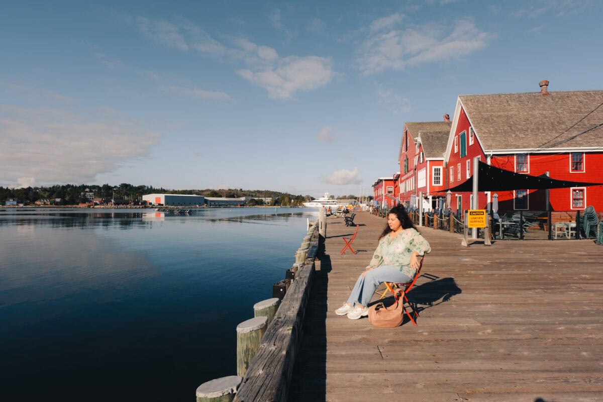 Frau sitzt auf Pier vor roten Gebäuden.