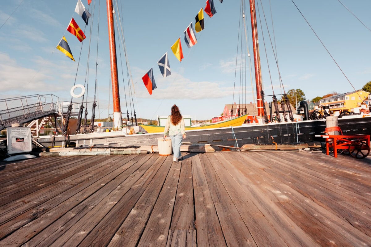 Person auf Holzpier vor Segelboot mit Flaggen.
