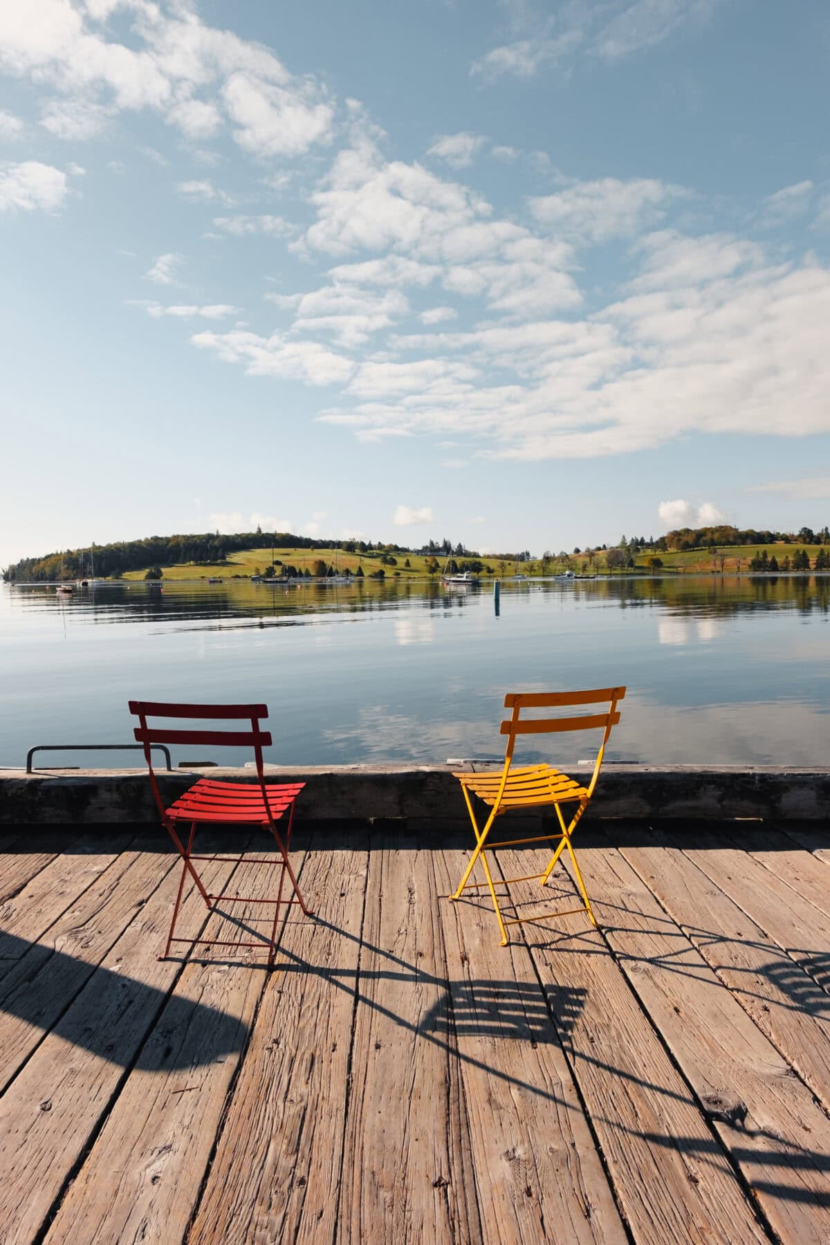 Zwei bunte Stühle auf einem Holzsteg am See.