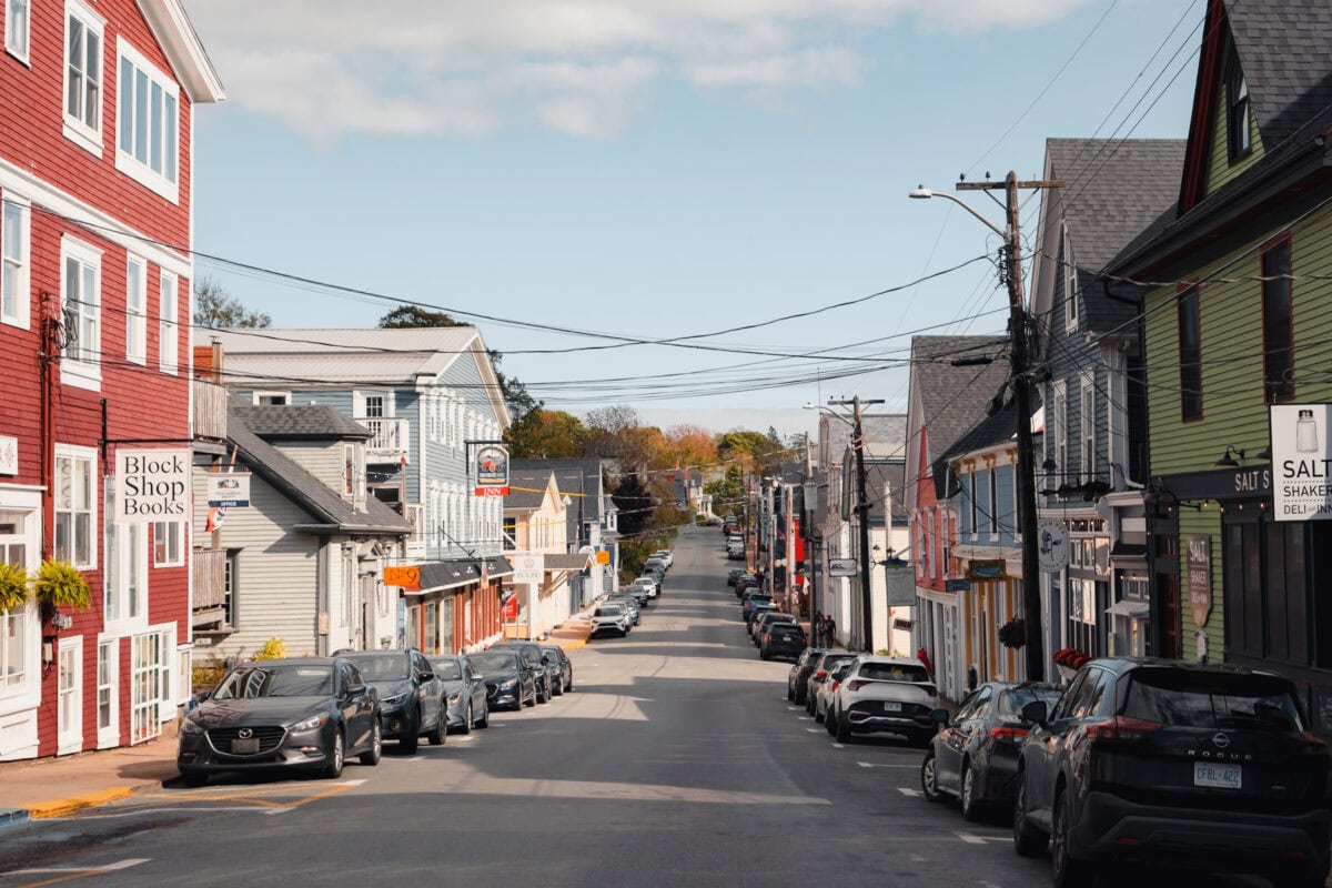 Kleine Stadtstraße mit geparkten Autos und Geschäften.