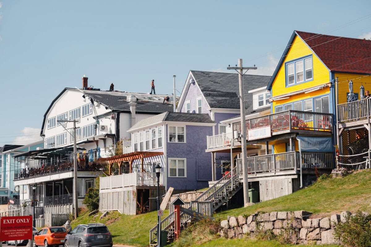 Bunte Häuserreihe am Hügel mit Handwerkern auf Dächern.
