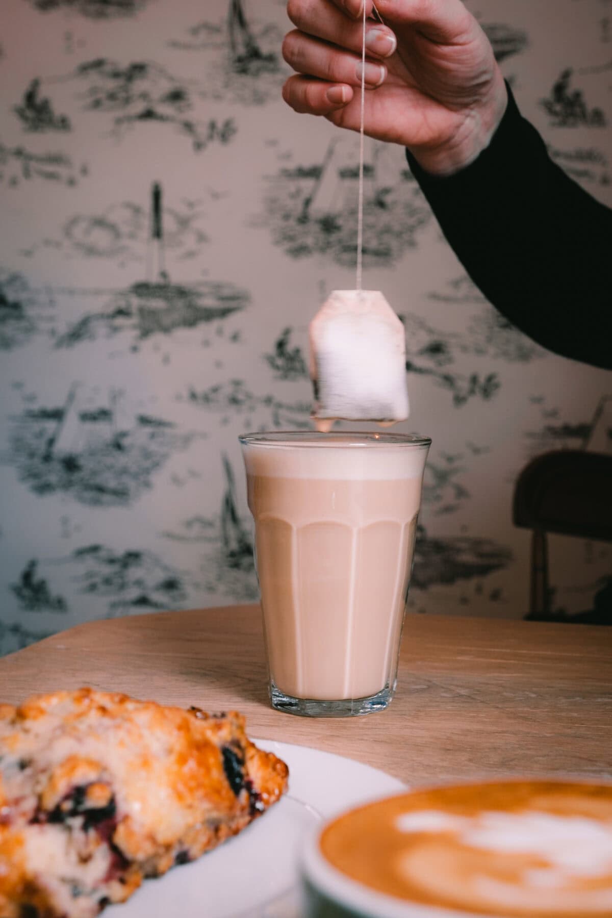 Hand hält Teebeutel über einem Milchkaffee.