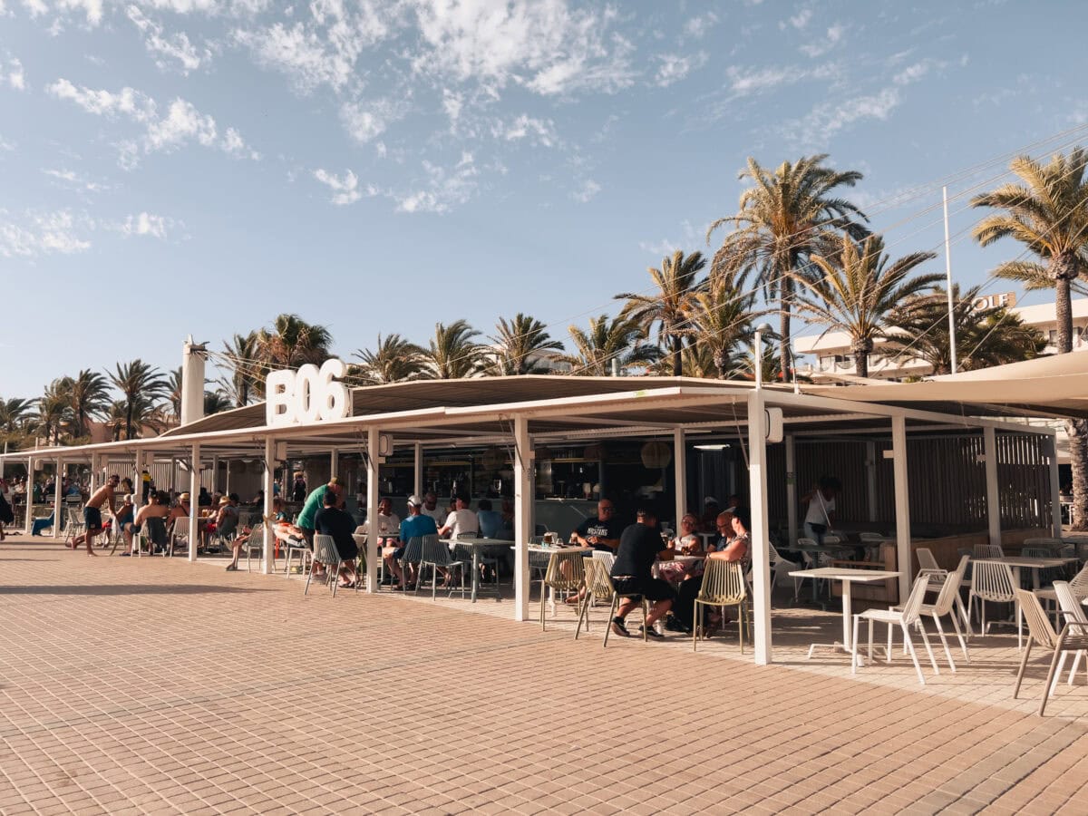 Strandbar mit Gästen unter Palmen.