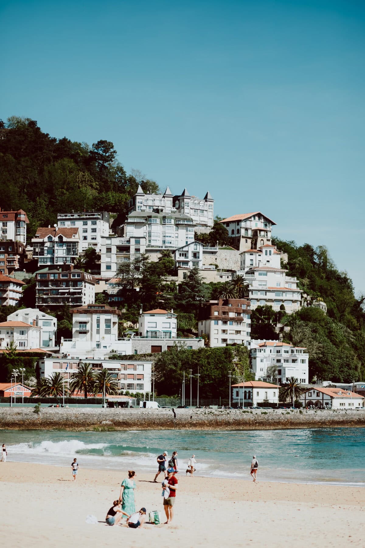 Strand mit Häusern auf Hügel im Hintergrund.