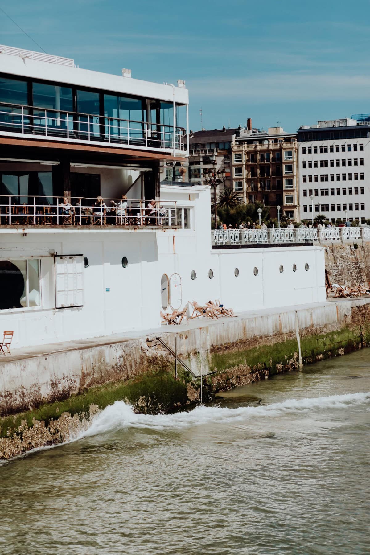 Weiße Fassade am Meer mit Balkon und Leuten