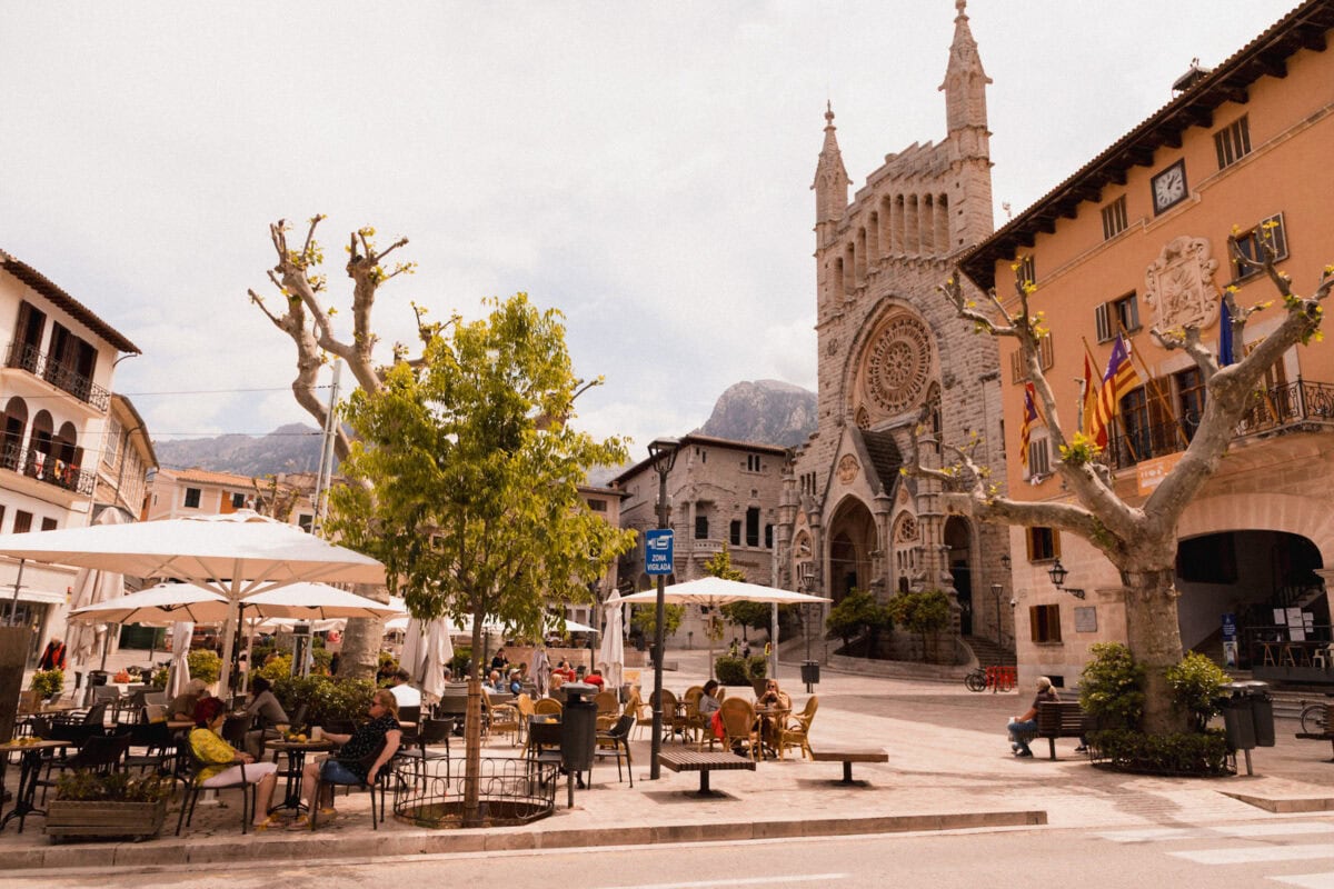Stadtplatz mit Kirche und Café-Terrasse im Freien.