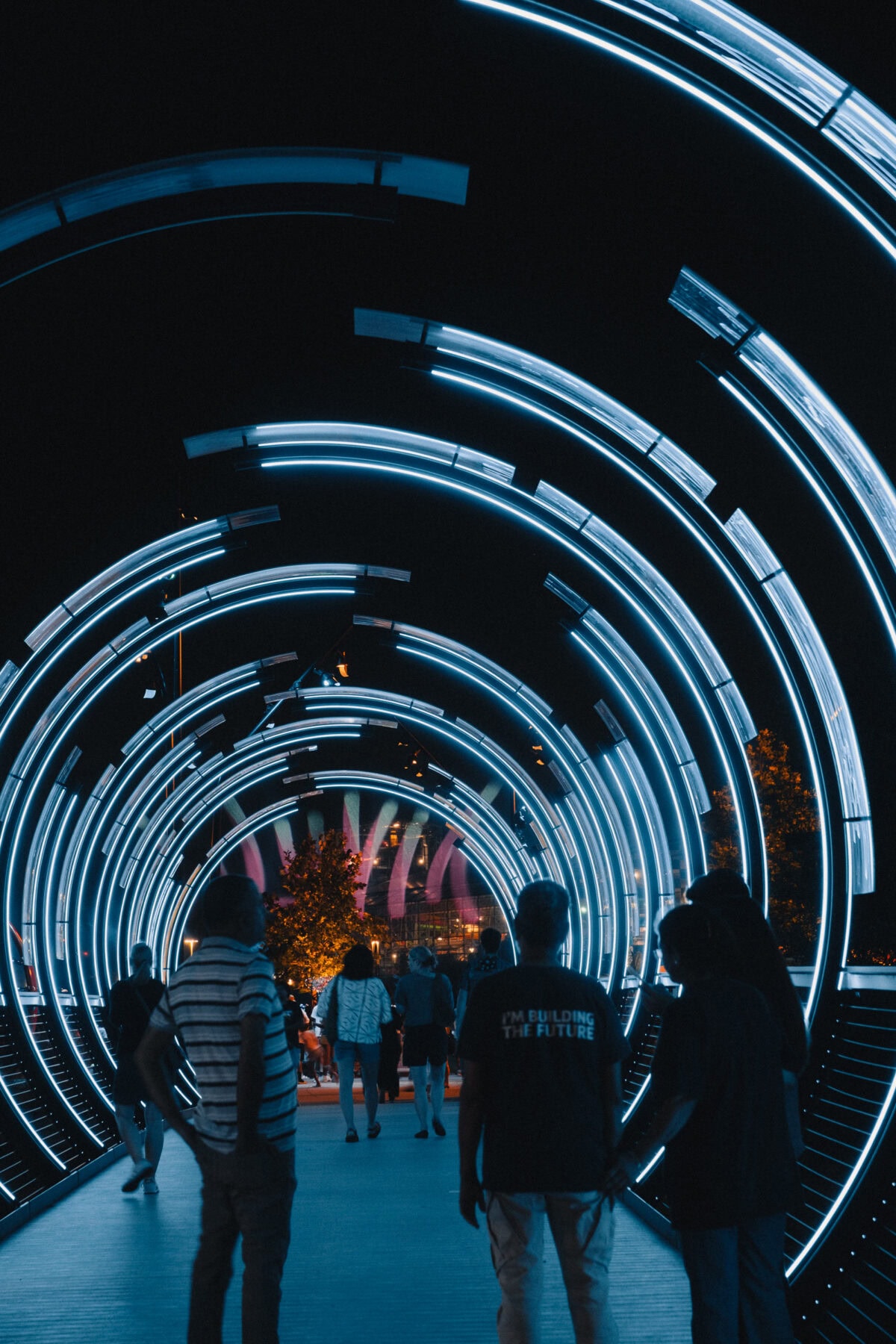 Menschen gehen durch futuristischen LED-Tunnel bei Nacht.