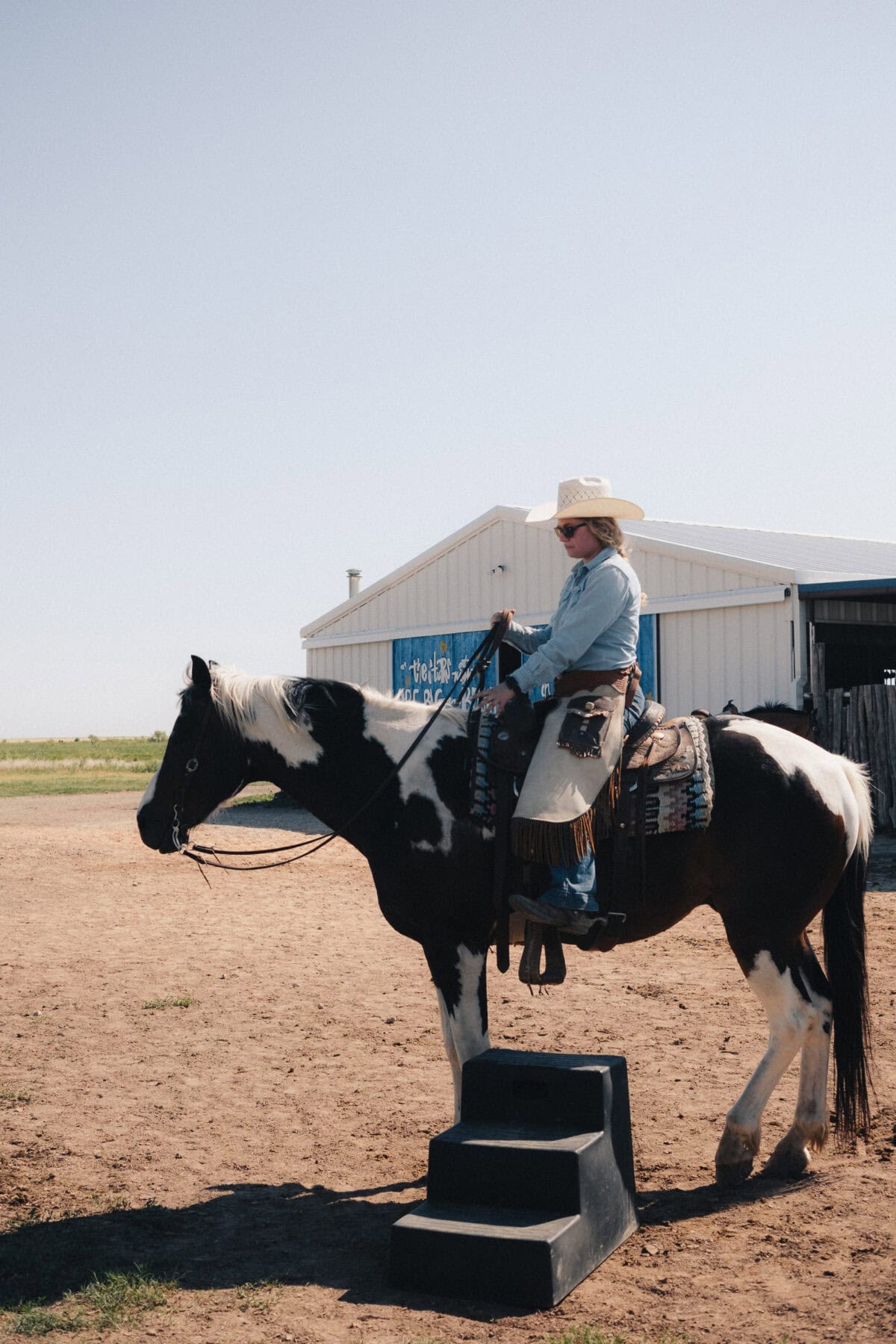 Cowgirl reitet auf geschecktem Pferd vor Scheune.
