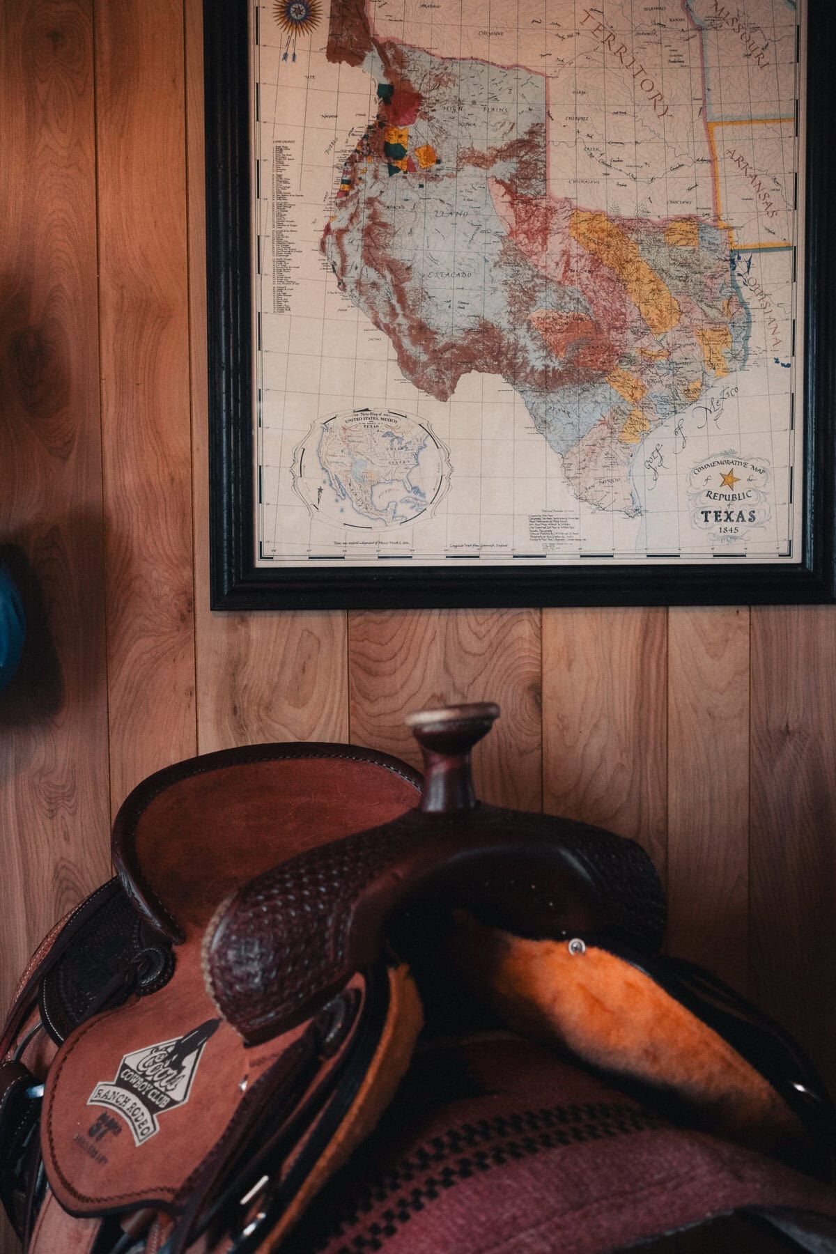 Sattel vor einer Texas-Karte an Holzwand.