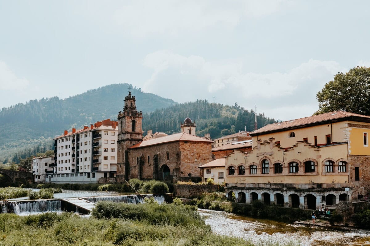 Historische Gebäude vor bewaldeten Hügeln und Fluss.