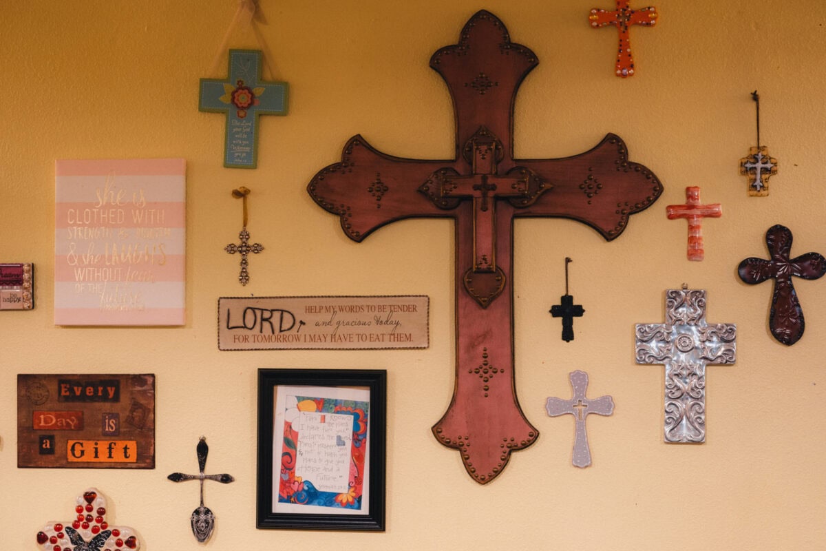 Verschiedene Wandkreuze und religiöse Schilder an gelber Wand.