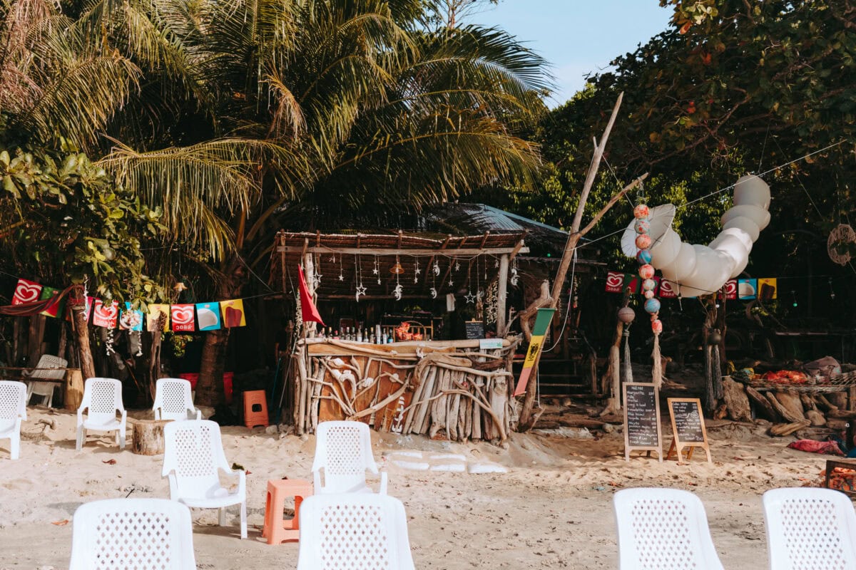 Rustikale Strandbar unter Palmen mit Plastikstühlen