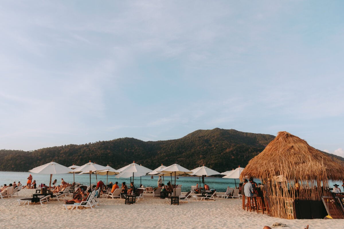 Belebter Sandstrand mit Sonnenschirmen und Strandbar