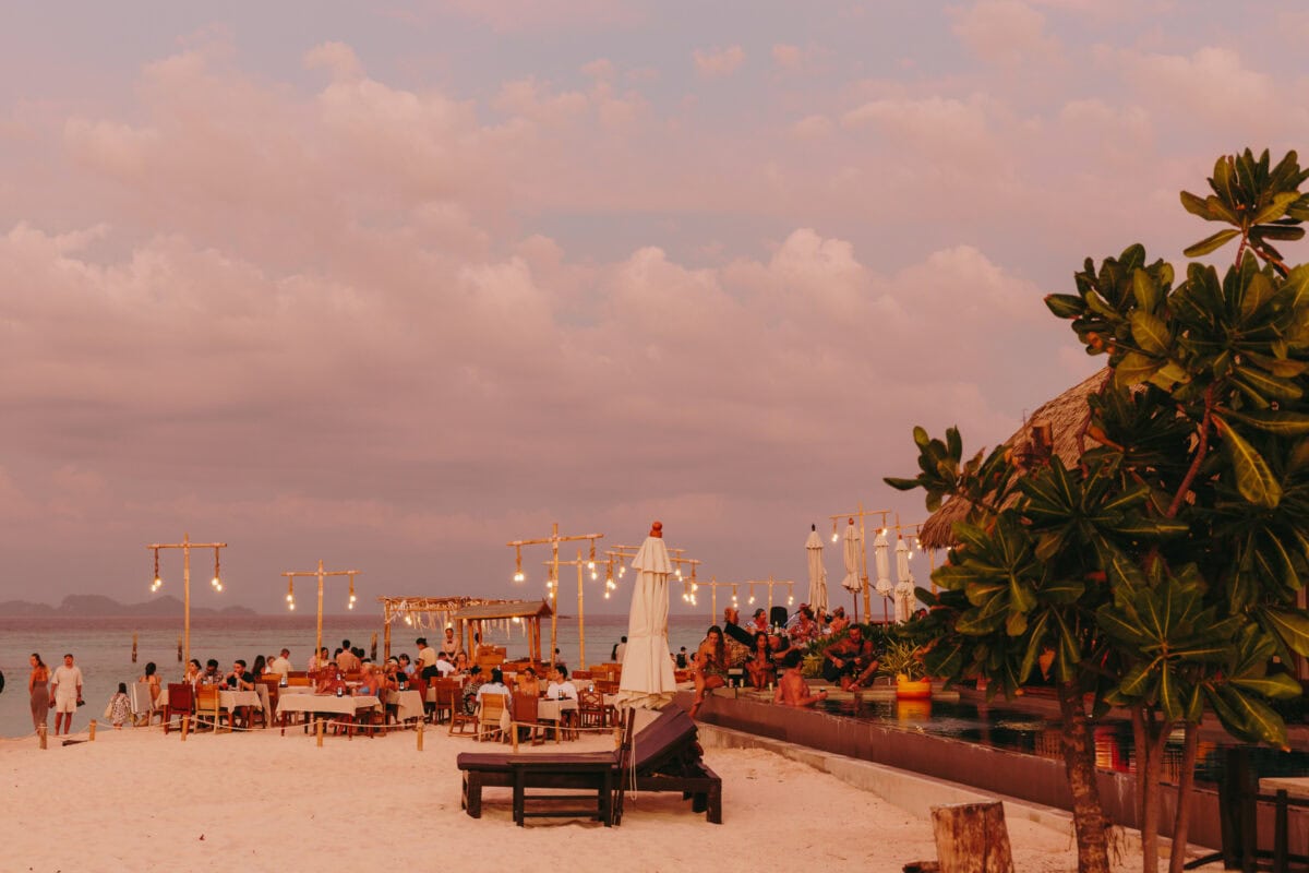 Strandrestaurant bei Sonnenuntergang mit Lichterketten und Gästen