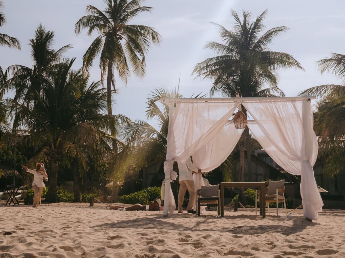 Strandpavillon mit weißen Vorhängen unter Palmen