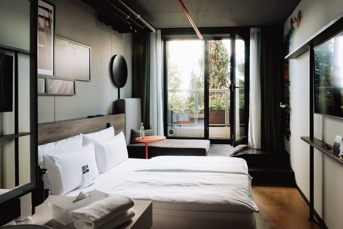 Modernes Hotelzimmer mit Balkon, Blick auf Bäume, helle Einrichtung, komfortabel.