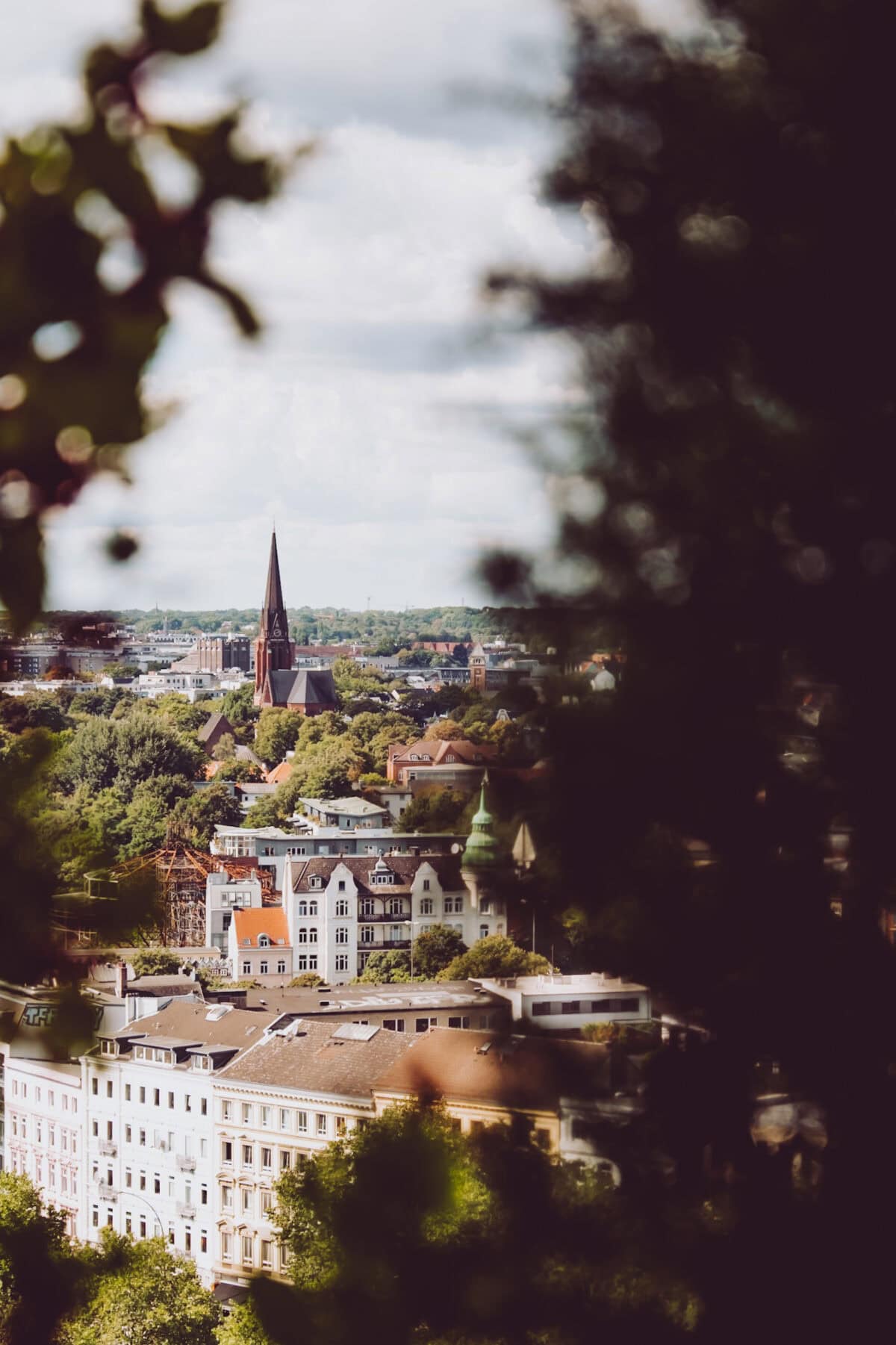 Blick auf Hamburgs Stadtzentrum mit Kirche im Hintergrund, umrahmt von Bäumen.