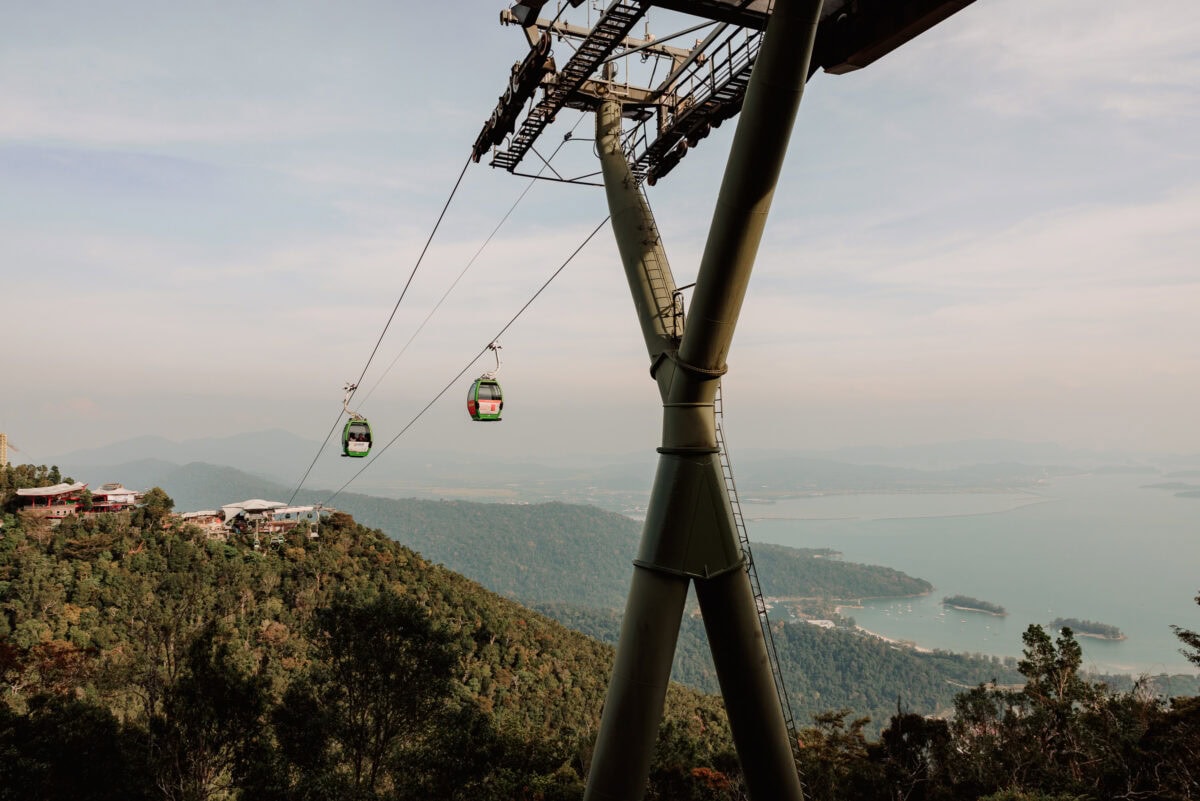 Seilbahngondeln über bewaldeten Bergen mit Meerblick