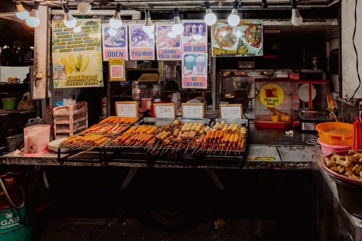 Malaysischer Straßenimbissstand mit Grillspießen und bunten Schildern