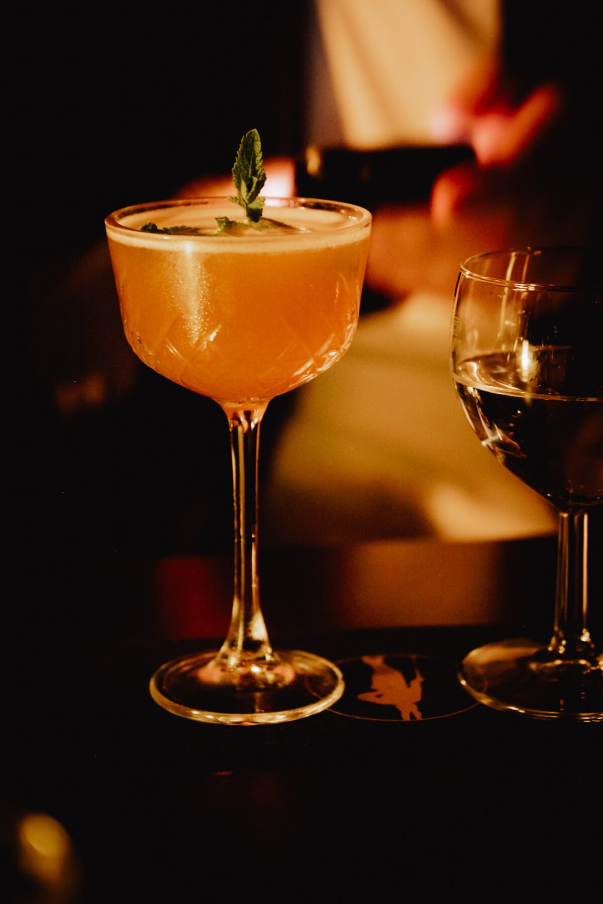 Orangefarbener Cocktail mit Minze in elegantem Coupeglas