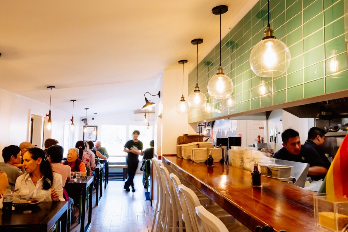 Belebtes Restaurant mit Theke, Hängeleuchten und grünen Fliesen