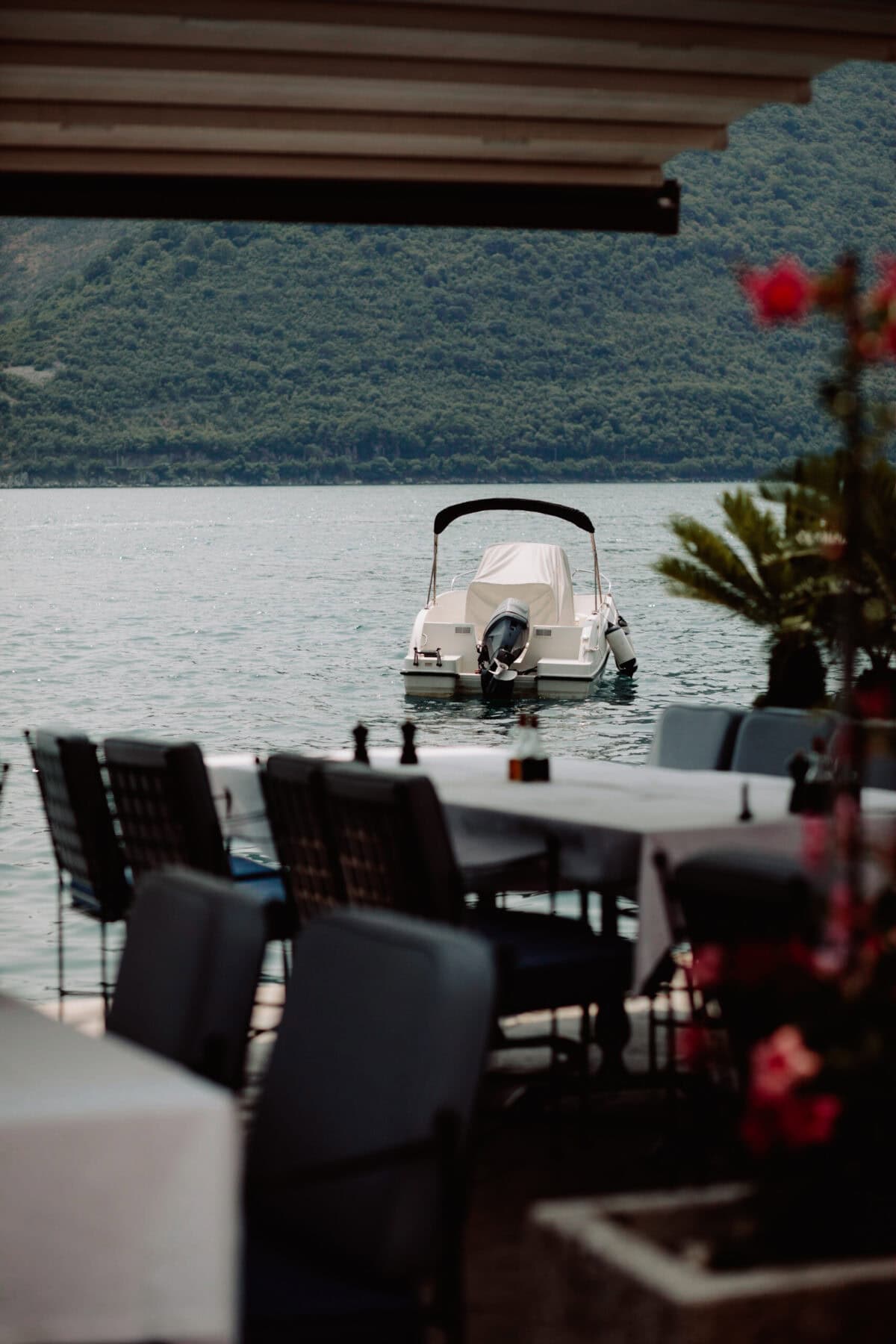 Restaurantterrasse am See mit weißem Boot und Bergen