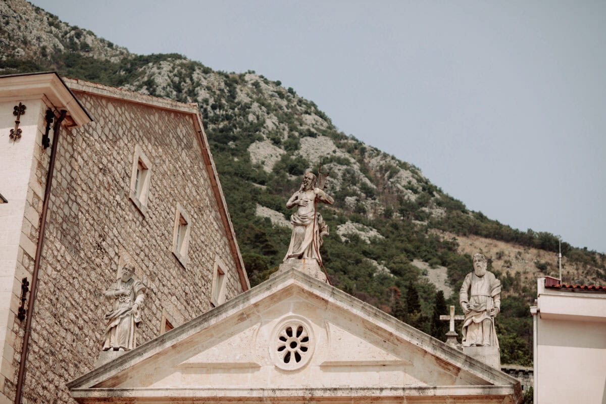Steinkirche mit religiösen Statuen vor bewaldeten Bergen